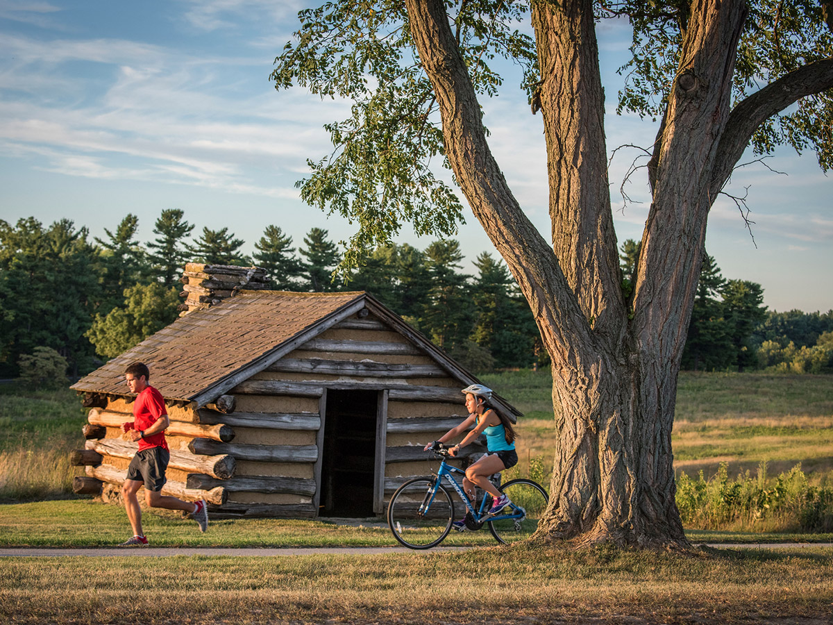 A man runs and a woman bikes through the trails of Valley Forge National Historical Park