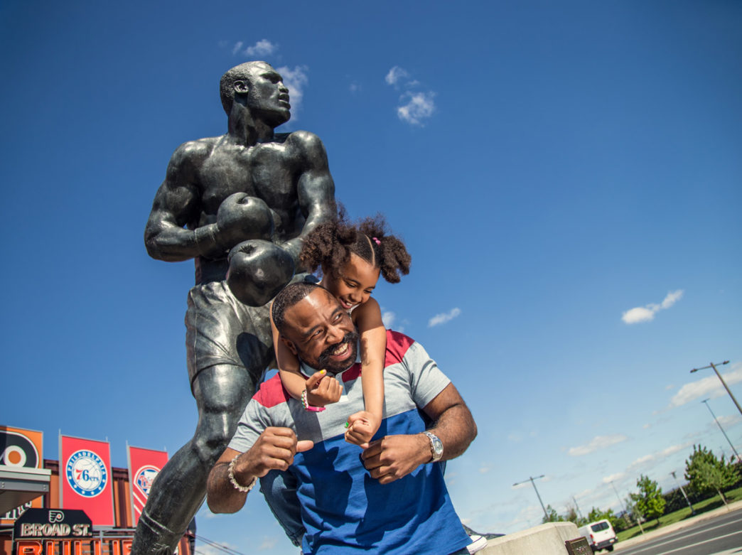 A father and daughter posing at the Joe Frazier statue at the South Philadelphia Sports Complex.