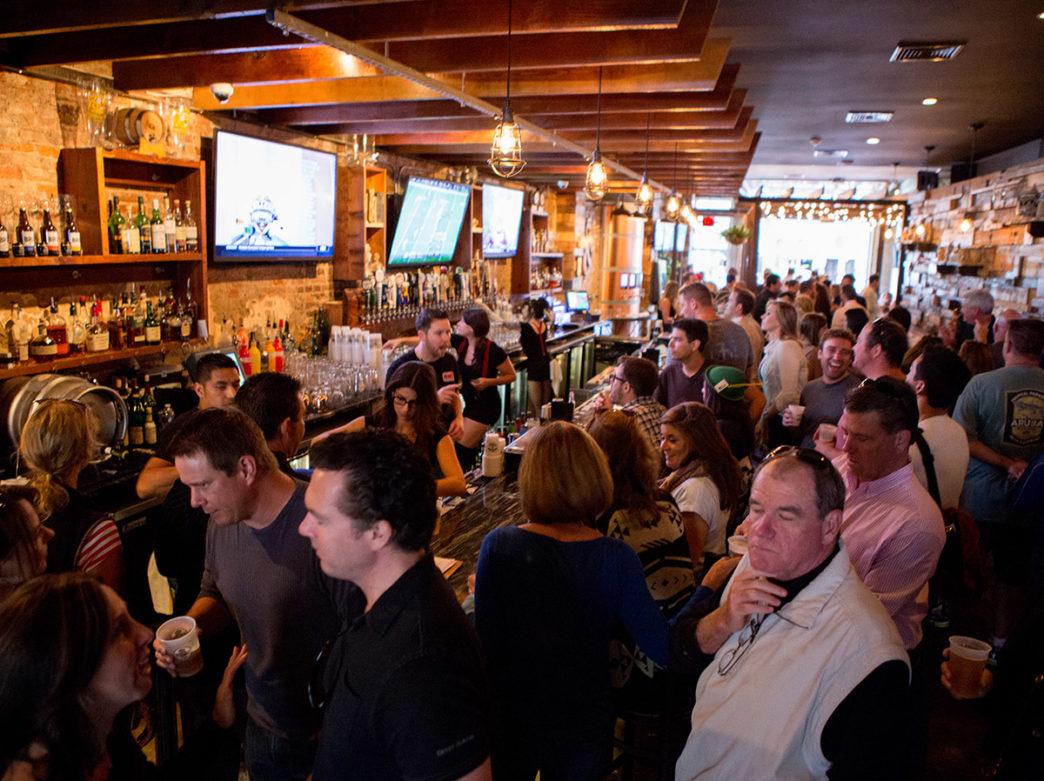 A crowd of people watches a game on TVs above the bar at BRU in Philadelphia