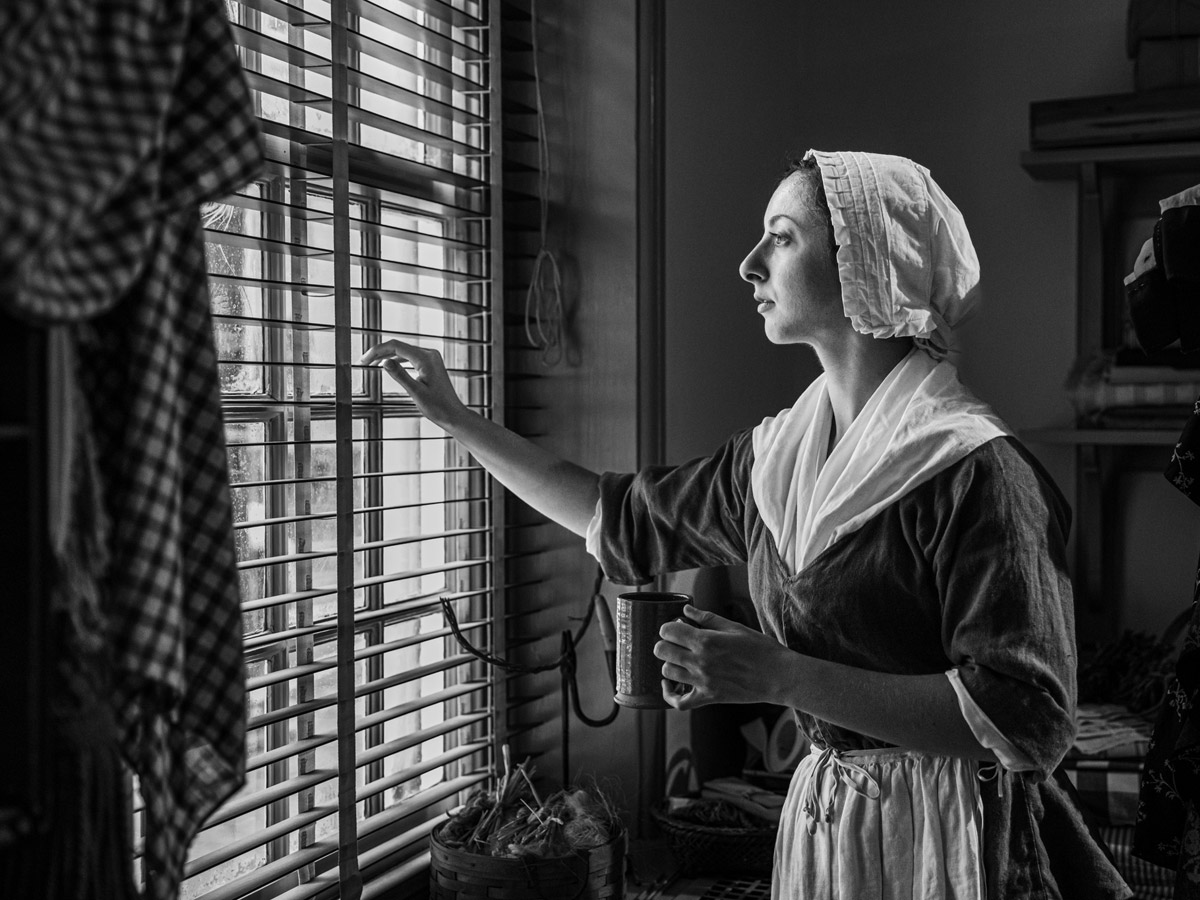 Woman peaking out a window during a spooky twilight tour at the Betsy Ross House