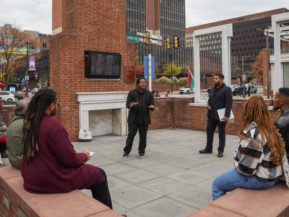 A tour guide from The Black Journey speaks to a group of seated tourgoers at The President's House in Philadelphia