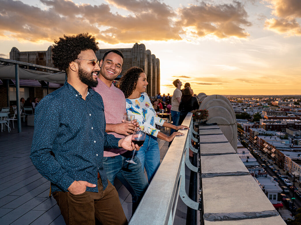 Three people enjoy drinks and look out at the view of the city while at Bok Bar rooftop.