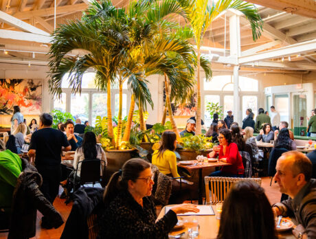 The dining room at Kalaya full with people dining. Palm trees as tall as the ceiling are in the center of the dining room.