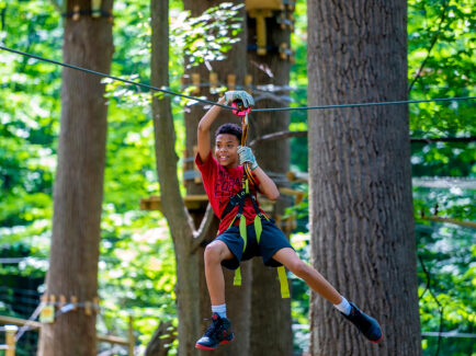 A kid wearing a harness rides the zipline at TreeTop Quest in Philadelphia.