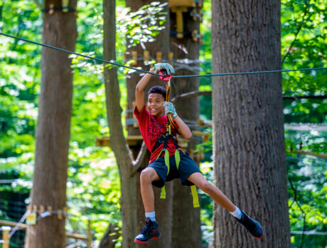 A kid wearing a harness rides the zipline at TreeTop Quest in Philadelphia.