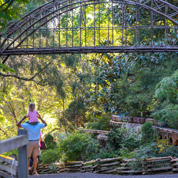 A father carries a child on their shoulders as they walk past the Garden Railway model trail at Morris Arboretum in Philadelphia.