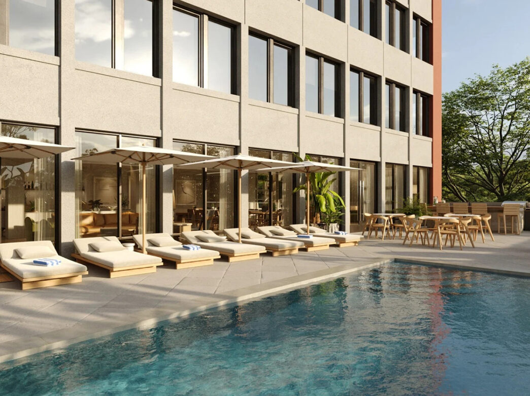 An outdoor pool is surrounded by lounge chairs with tan cushions, umbrellas and dining tables at the ROOST Kelly Drive.