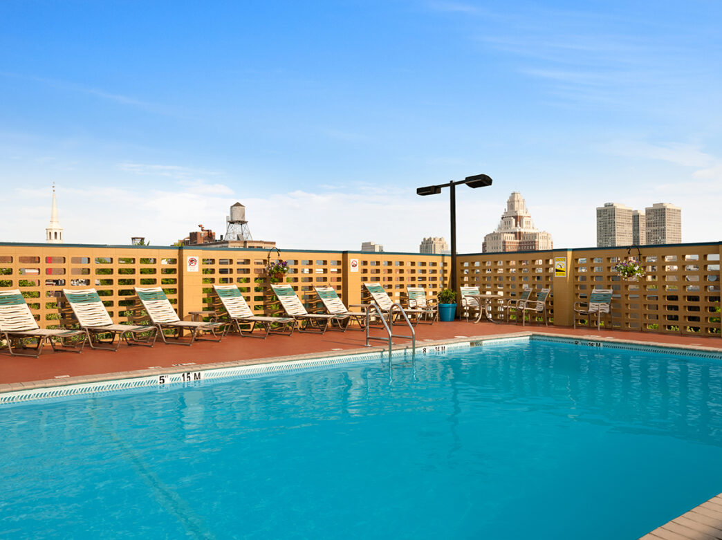 An outdoor pool is surrounded by a tan privacy wall and white lounge chairs at the Wyndham Philadelphia Historic District.
