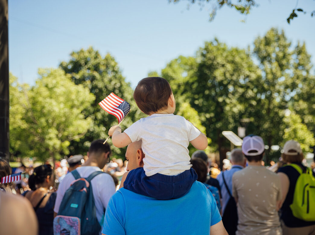 A young child sits on their father's shoulders while holding a mini American flag while attending the Independence Day Parade in Philadelphia.