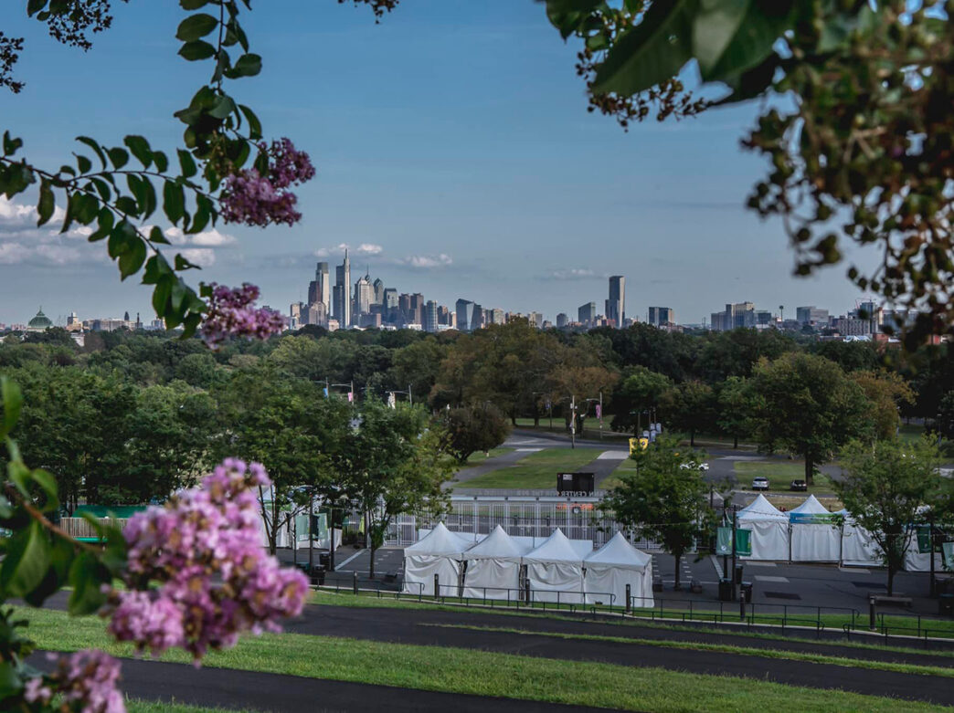 A view of the Philadelphia skyline framed by greenery and purple flowers overlooking the entrance to The Mann Center.