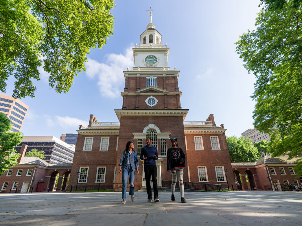 Three people walk with the back of Philadelphia's Independence Hall in the background