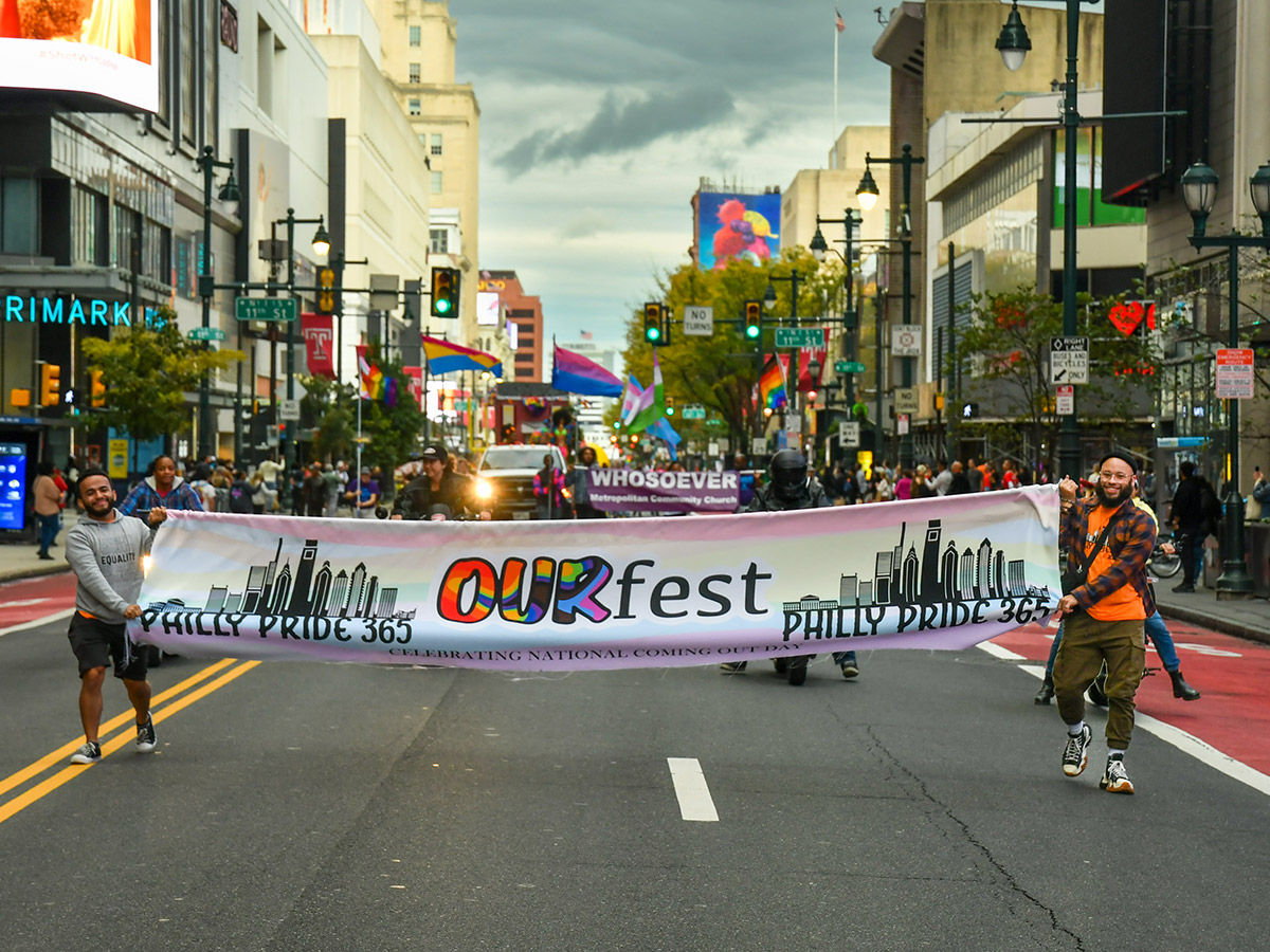 OURfest parade-marchers carrying a banner leads the parade through Center City. The banner reads "Philly Pride 365, OURfest, Celebrating National Coming Out Day."