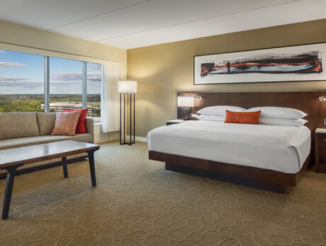 A modern hotel room featuring a king-size bed with crisp white linens, a seating area with a plush couch and coffee table, and floor-to-ceiling windows showcasing scenic views.