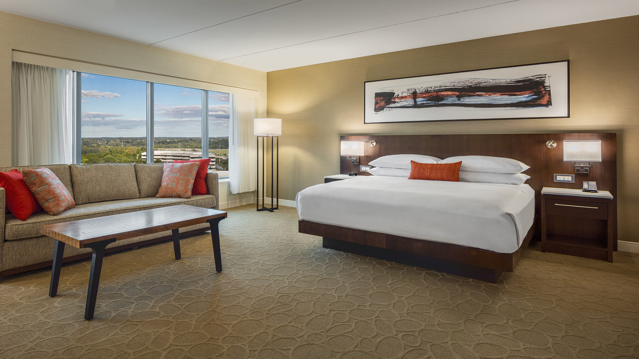 A modern hotel room featuring a king-size bed with crisp white linens, a seating area with a plush couch and coffee table, and floor-to-ceiling windows showcasing scenic views.