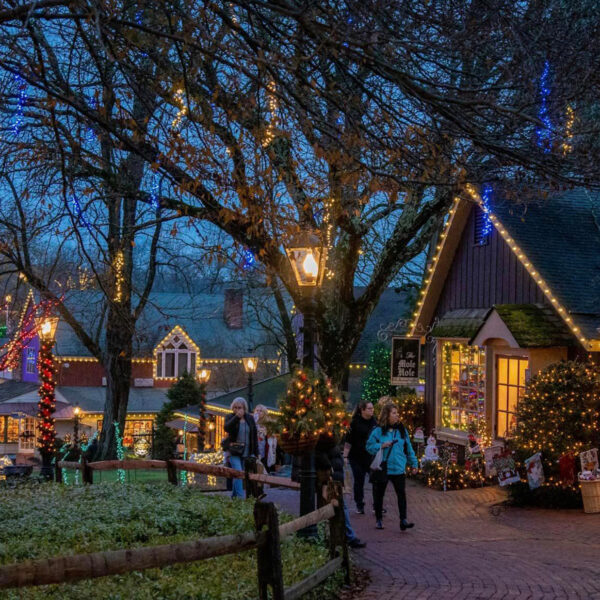 People strolling through Peddler's Village with holiday lights decorating the trees and buildings.