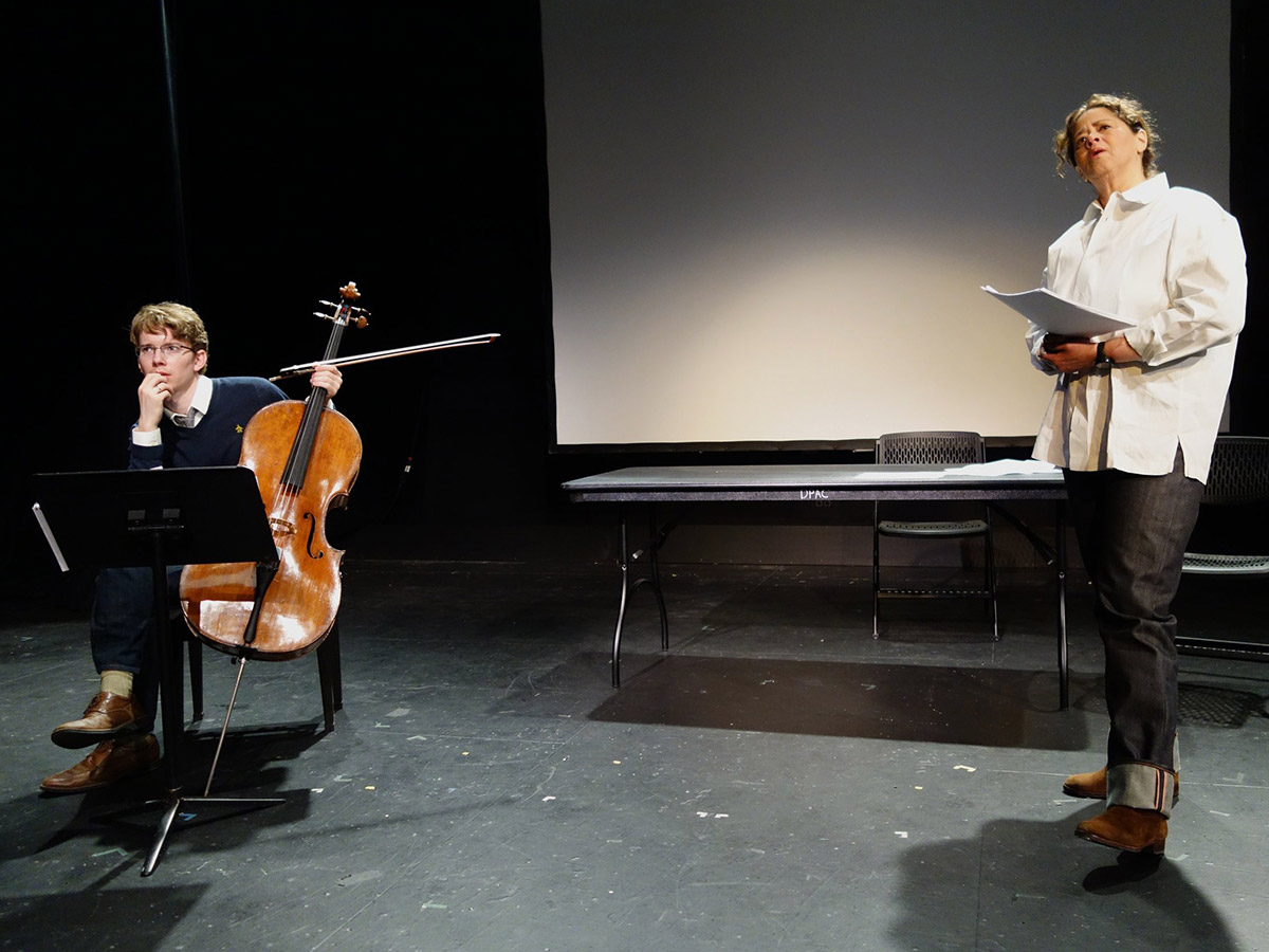 Playwright Anna Deavere Smith, dressed in a white button-up and jeans, stands onstage with cellist Joshua Roman.