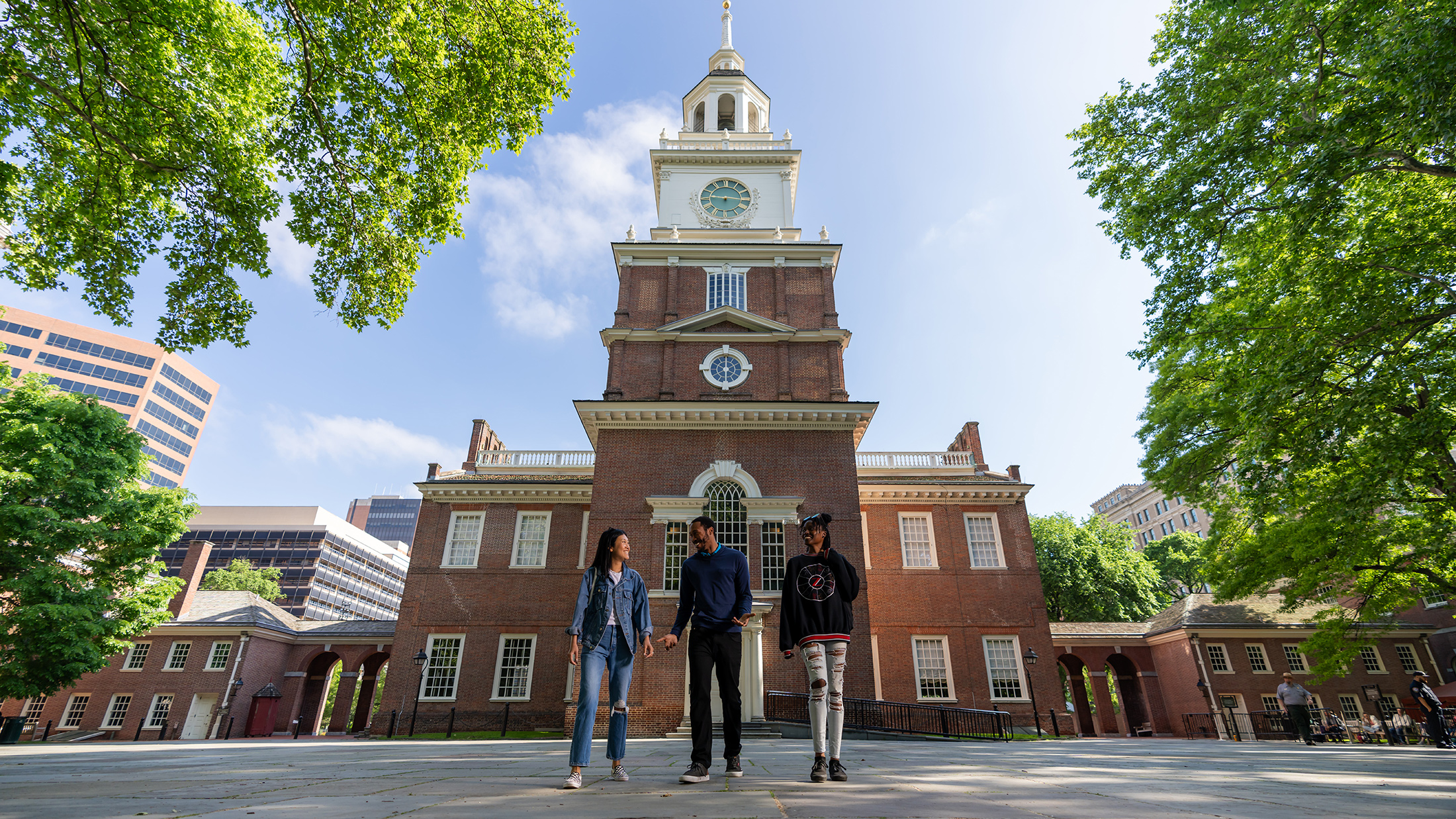 Three people walk with the back of Philadelphia's Independence Hall in the background.