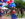 People walking in a parade line holding colorful balloons during Red, White & Blue To-Do. A woman waves at the camera