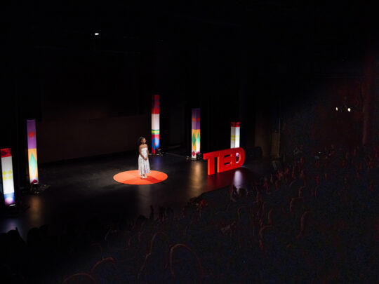 A speaker on a stage in a spotlight during a TED Democracy event in Philadelphia