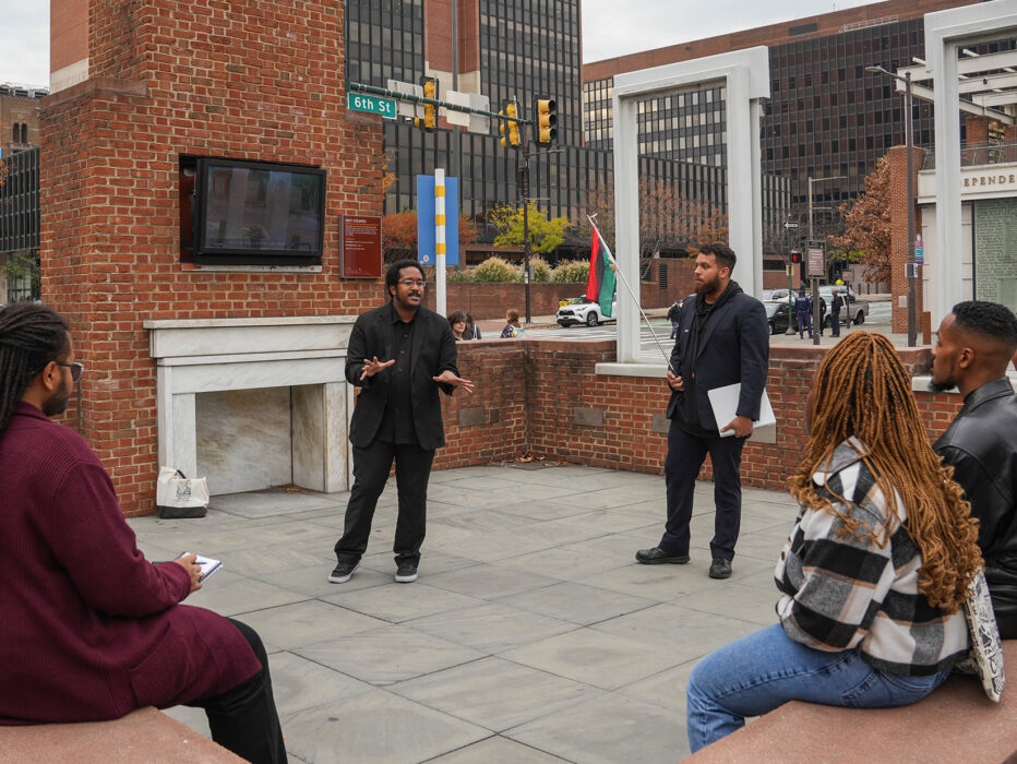 A tour guide from The Black Journey speaks to a group of seated tourgoers at The President's House in Philadelphia