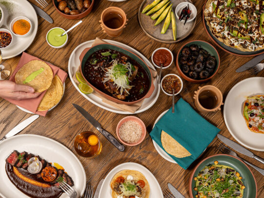A variety of Mexican dishes, including tortillas, a tuna tostada and carne asada, sit on a wooden table at Amá