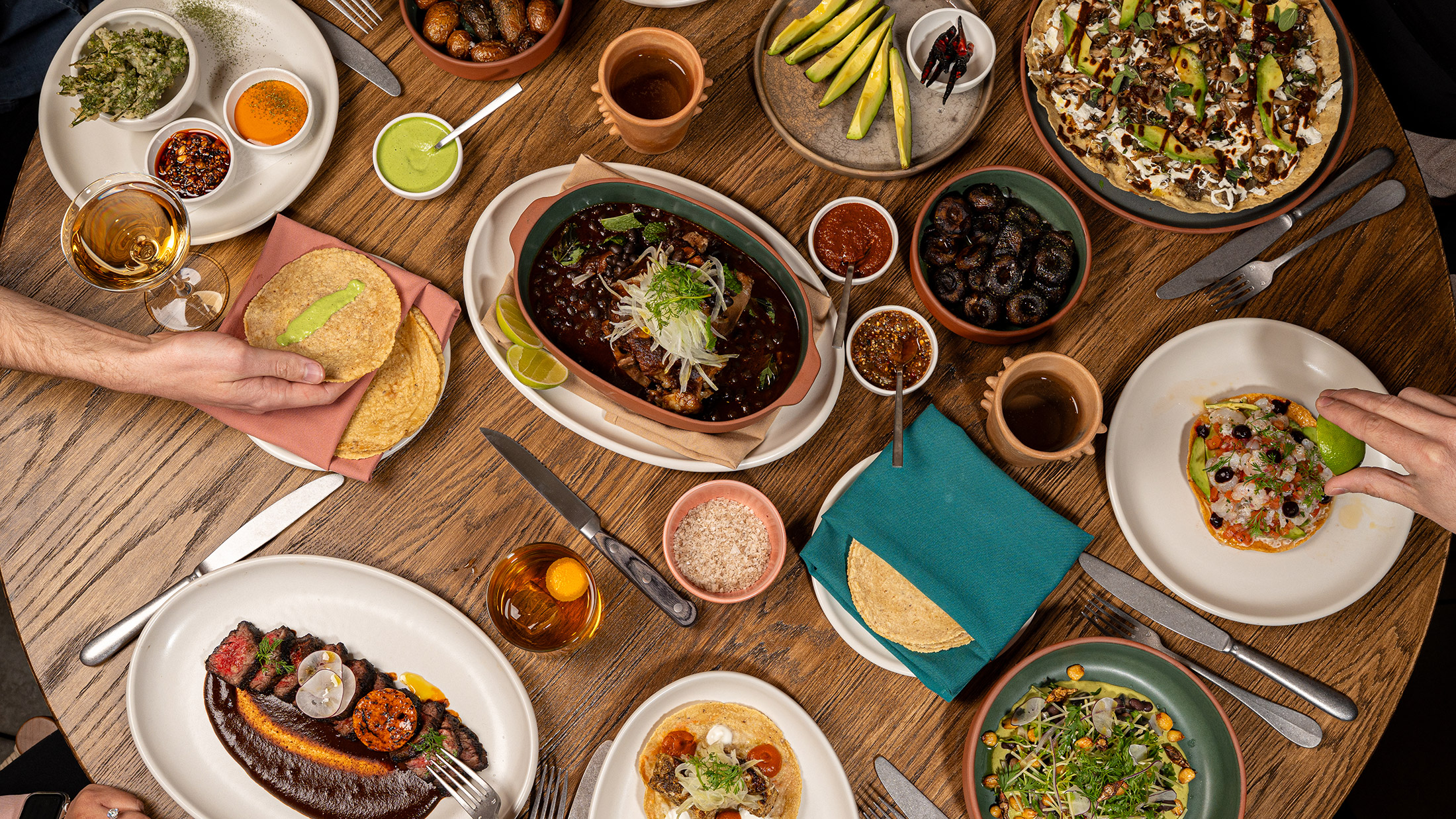 A variety of Mexican dishes, including tortillas, a tuna tostada and carne asada, sit on a wooden table at Amá