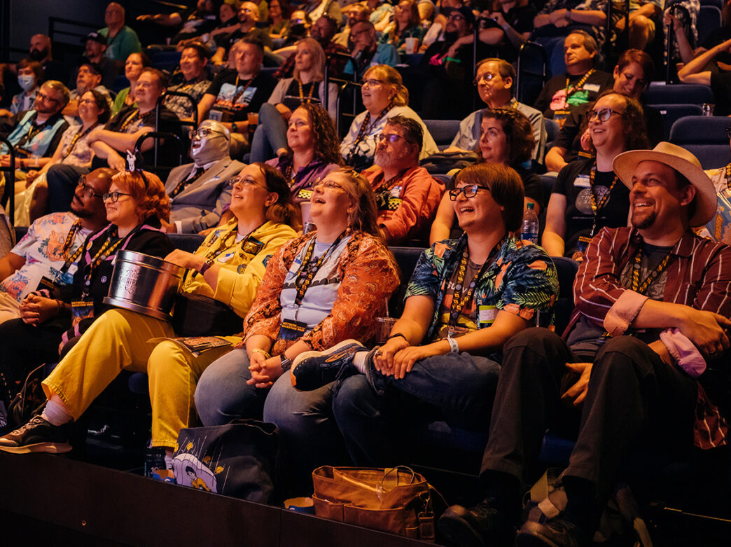 A lively audience dressed in colorful and quirky outfits watches a performance at Blobfest at The Colonial Theatre. The crowd laugh and smile under warm lighting.