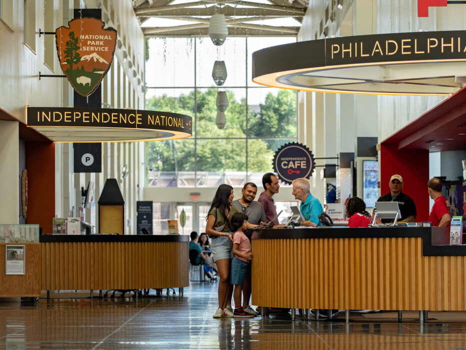 People stand at an information desk and speak to a staff member in Philadelphia Independence Visitor Center.