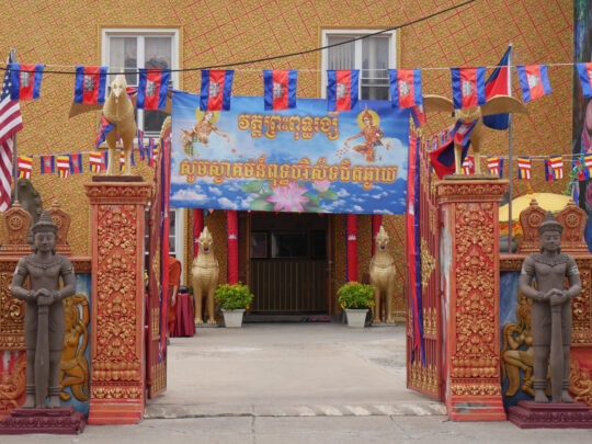 The exterior the Preah Buddha Rangsey Temple in Philadelphia, with a red and orange gate entrance decorated with bronze and gold statues.