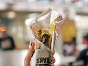 A hand holds up a cheesesteak wrapped in paper at Geno's Steaks.