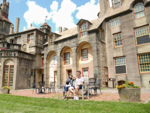 Two people sit on a bench on a clear blue day with the Fonthill Castle in the background.