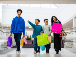 A family walks through King of Prussia mall pointing at stores and holding colorful shopping bags.