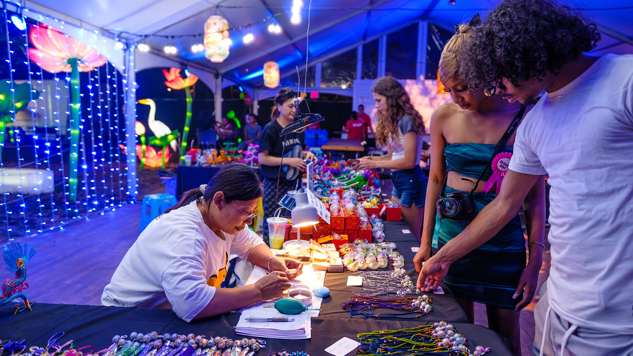 Two people browse arts and crafts at a folk vendor table inside a large tent at the Chinese Lantern Festival.