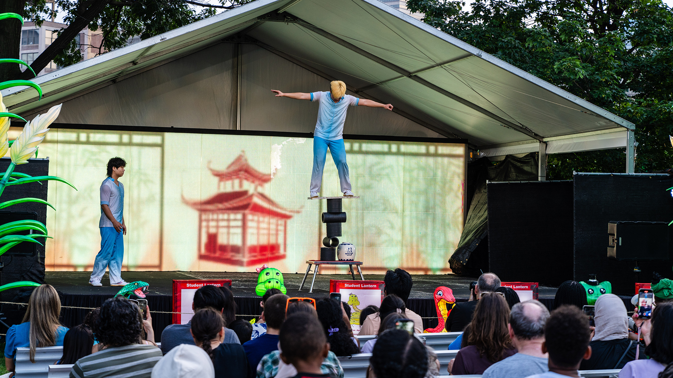 A performer balances on a stack of cylinders during a live acrobatic show in front of a crowd of people at the Chinese Lantern Festival.