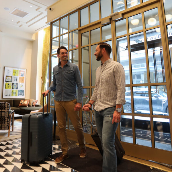 Two people with suitcases walk through glass doors into the lobby at Canopy by Hilton Philadelphia.