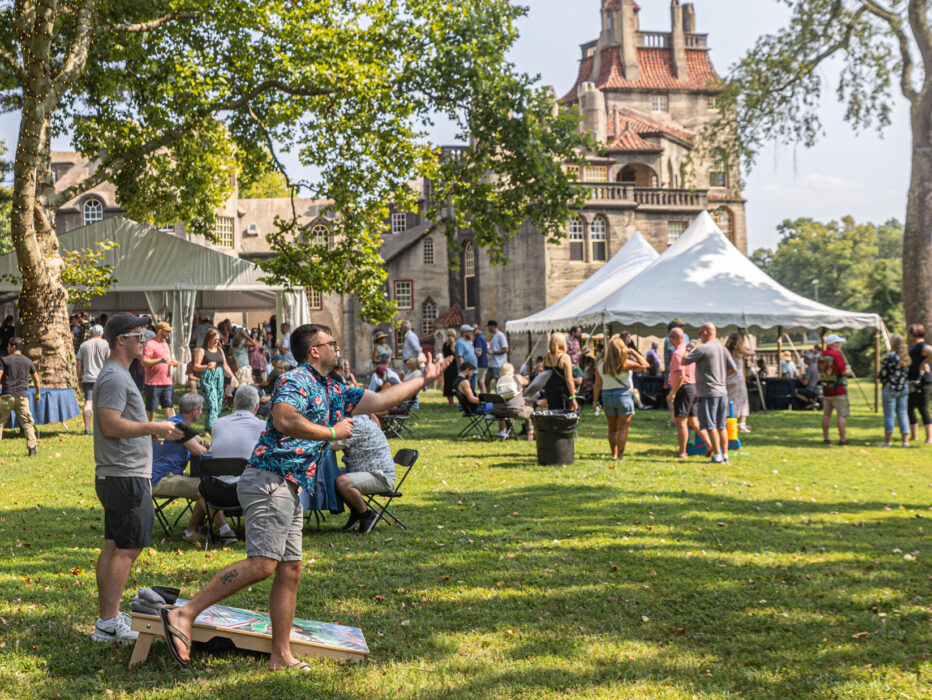 Festivalgoers sip drinks and play lawn games beneath shady trees on a grass lawn in front of Fonthill Castle during the annual beer fest.